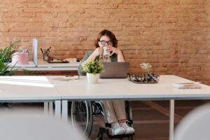 Femme en fauteuil roulant travaillant sur un ordinateur portable dans un espace de bureau lumineux. Crédit photos : Marcus Aurelius sur Pexels