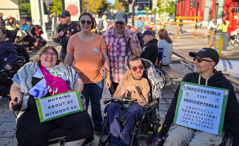 Cinq membres du GAPA, souriants, à la manifestation pour l'accessibilité universelle, à Montréal, le 3 octobre 2026. À l'avant : Léo Gauthier et François Bernier en fauteuil roulant motorisé, et Jérôme Saunier, en fauteuil roulant manuel. Derrière, debout : Élisa Thibault et Jérôme Plante, qui tient une canne blanche. Deux pancartes : « Nothing about us without us! » et « Inaccessible, c'est inacceptable! »